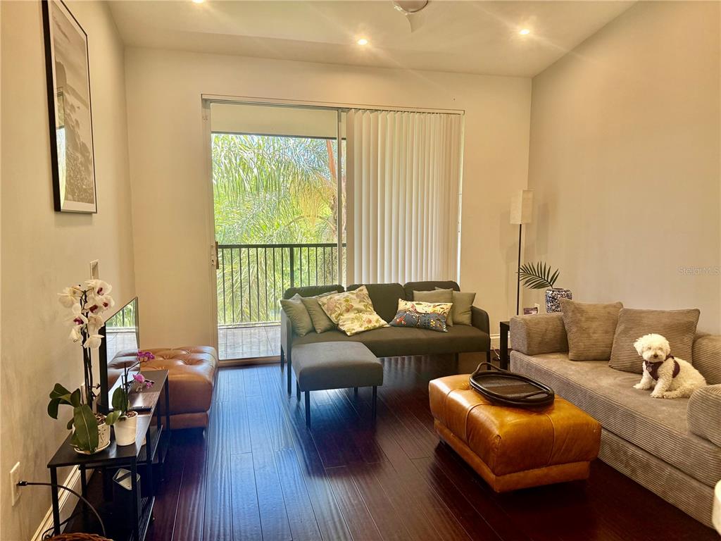 A living room features dark wood floors, two sofas, a leather ottoman, and a balcony door — 1180 RESERVE WAY UNIT 302, NAPLES, FL