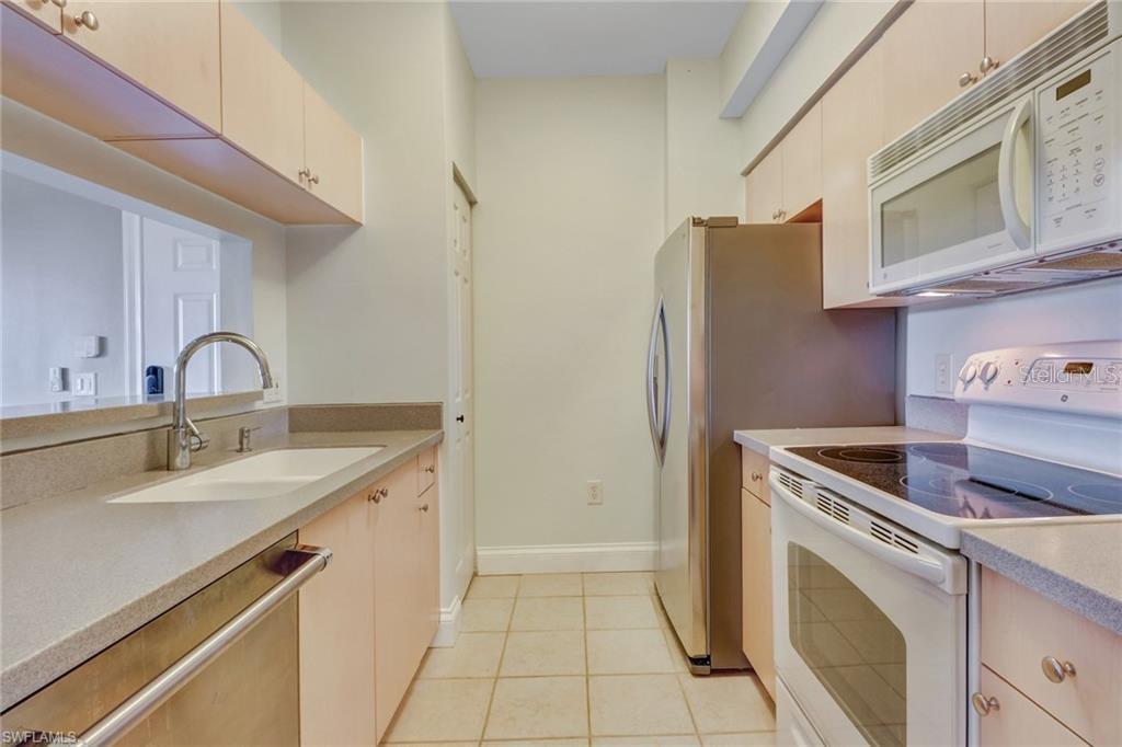 A galley kitchen features light wood cabinets, stainless steel appliances, and a white tiled floor — 1180 RESERVE WAY UNIT 302, NAPLES, FL