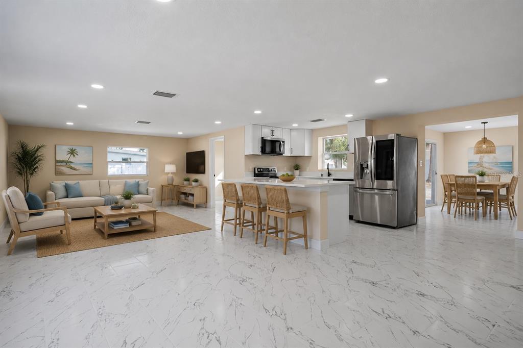 An open-concept living room and kitchen with white marble-look tile flooring and stainless steel appliances — 6211 CORNELL ROAD, BRADENTON, FL
