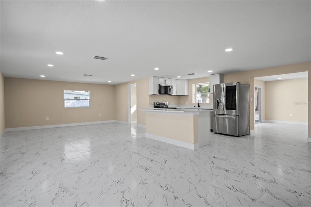 An open-concept kitchen and living area with white marble-look tile flooring and stainless steel appliances — 6211 CORNELL ROAD, BRADENTON, FL
