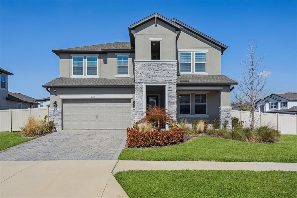 A two-story suburban house with a gray stucco exterior, stone accents, and a paved driveway — 33287 SYCAMORE LEAF DRIVE, WESLEY CHAPEL, FL