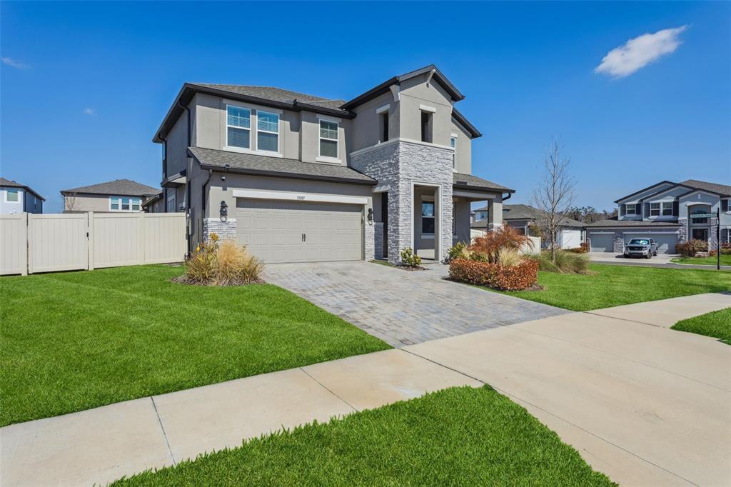 A two-story suburban house features a stone facade, a two-car garage, and a paved driveway — 33287 SYCAMORE LEAF DRIVE, WESLEY CHAPEL, FL