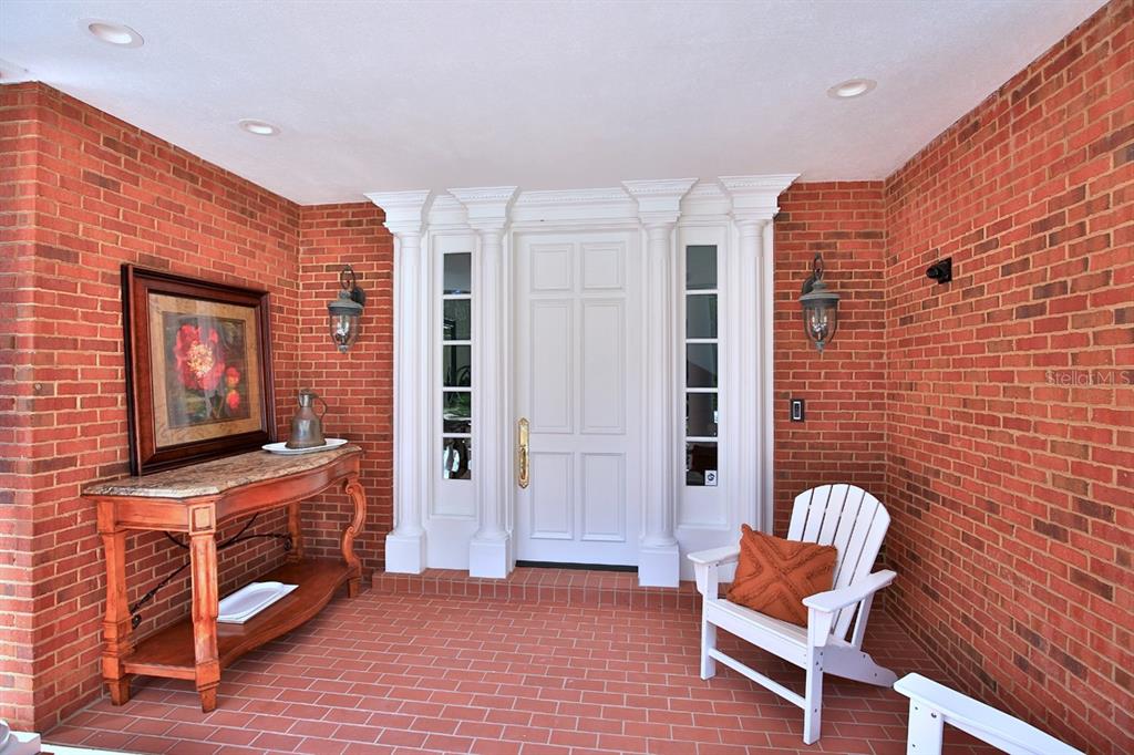 A brick-walled front porch features a white door with sidelights, a wooden console table, and chairs — 1401 SE 91ST PLACE, OCALA, FL