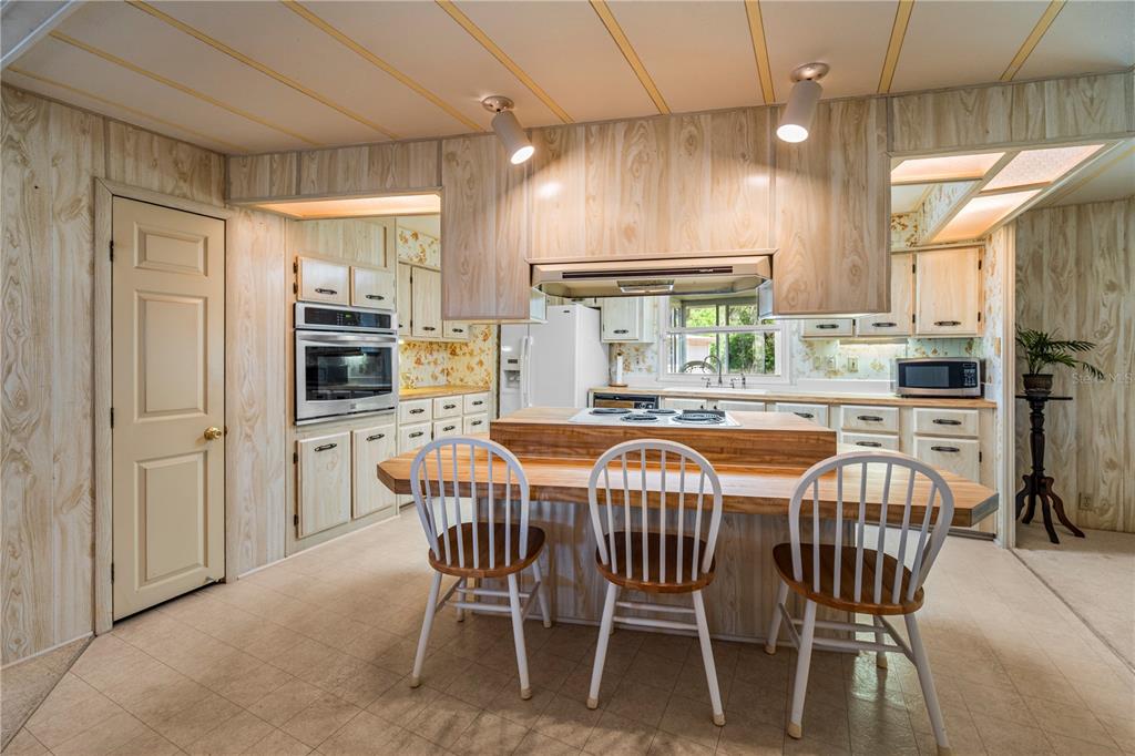 A kitchen with wood-paneled walls, a central island with seating, and a built-in wall oven — 2513 INDEPENDENCE LANE, ST CLOUD, FL