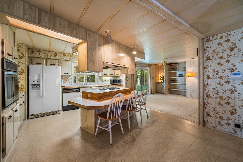 A kitchen with wood-paneled cabinets and a central island flows into a carpeted living area — 2513 INDEPENDENCE LANE, ST CLOUD, FL