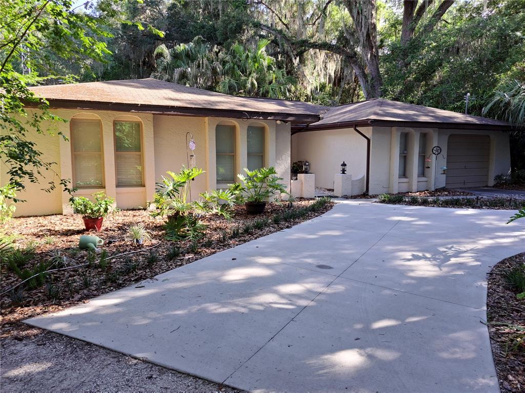 A single-story house with a beige stucco exterior, a concrete driveway, and surrounding trees — 5672 AVE H, MC INTOSH, FL