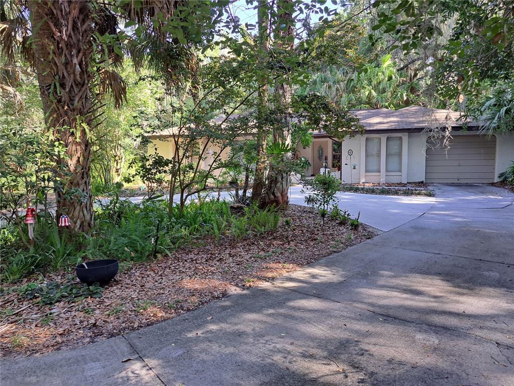 A single-story house with a concrete driveway and garage sits behind trees and landscaping — 5672 AVE H, MC INTOSH, FL