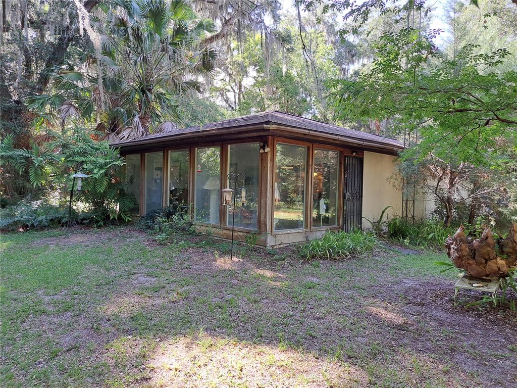 A detached, flat-roofed structure with large glass windows sits in a wooded, grassy yard — 5672 AVE H, MC INTOSH, FL
