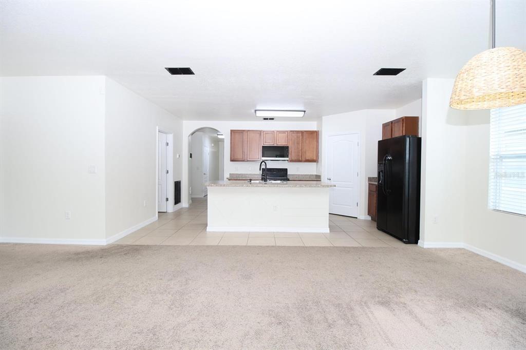 A kitchen with wooden cabinets, a central island, and black appliances overlooks a carpeted living area — 3238 BAYOU BAY DRIVE, LAKELAND, FL