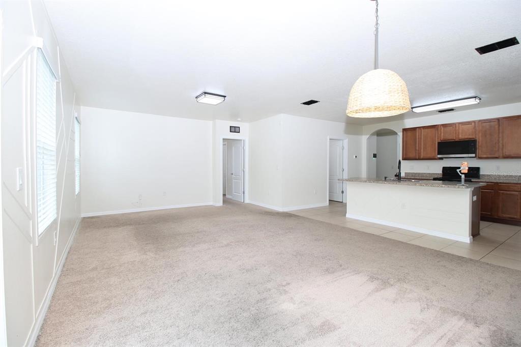 A spacious living room with beige carpet opens to a kitchen with wooden cabinets — 3238 BAYOU BAY DRIVE, LAKELAND, FL