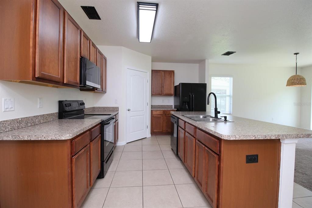 A kitchen with wood cabinets, laminate countertops, black appliances, and a central island — 3238 BAYOU BAY DRIVE, LAKELAND, FL