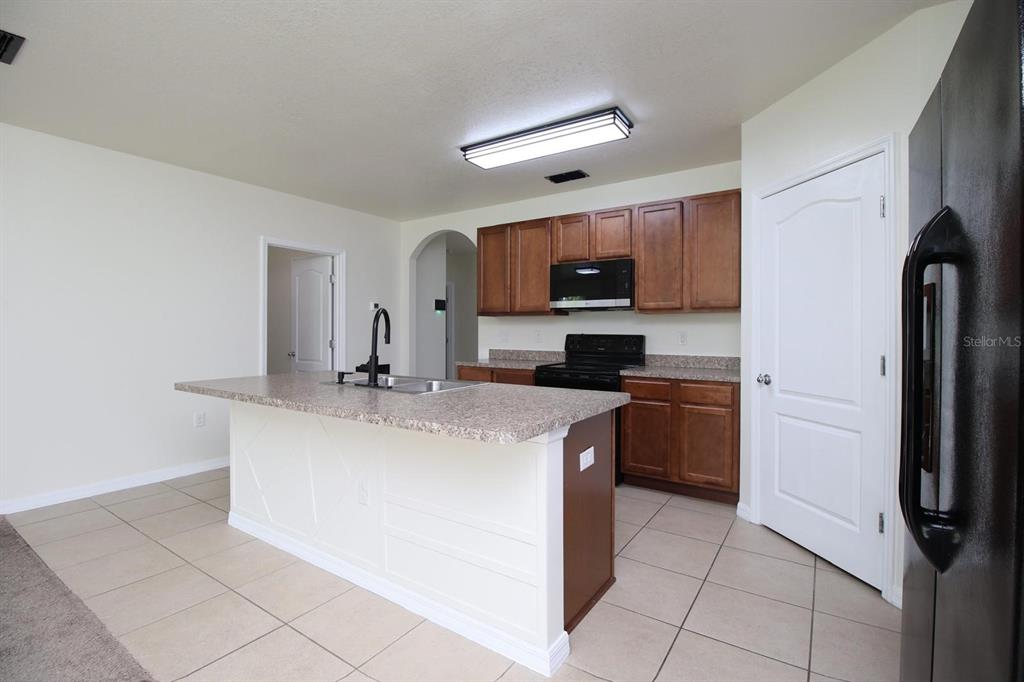A kitchen with a central island, brown cabinets, black appliances, and light-colored tile flooring — 3238 BAYOU BAY DRIVE, LAKELAND, FL