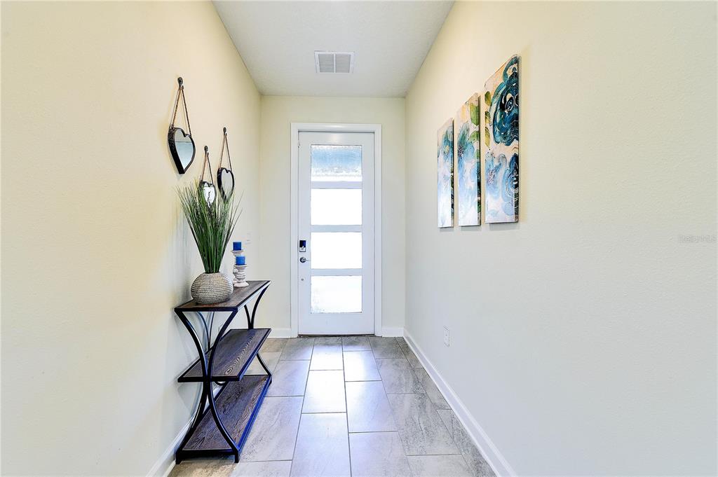 A bright entryway features tile flooring, a console table, wall art, and a glass-paneled door — 8974 CABOT CLIFFS DRIVE, DAVENPORT, FL