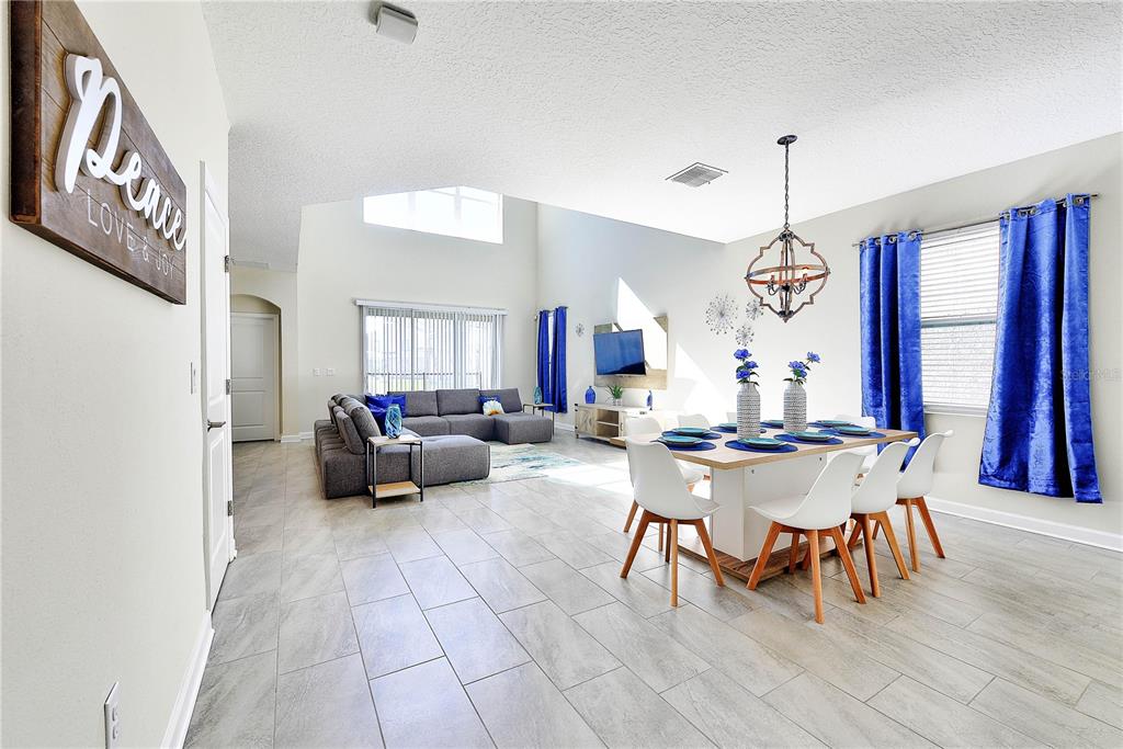 An open-concept living and dining area features tile flooring, vaulted ceilings, and blue curtains — 8974 CABOT CLIFFS DRIVE, DAVENPORT, FL