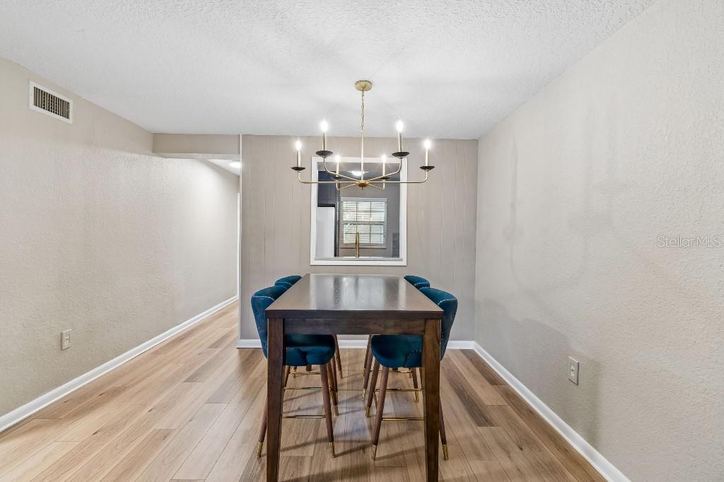 A dining room features a dark wood table, blue velvet chairs, and a brass chandelier — 2500 LEE ROAD UNIT 104, WINTER PARK, FL