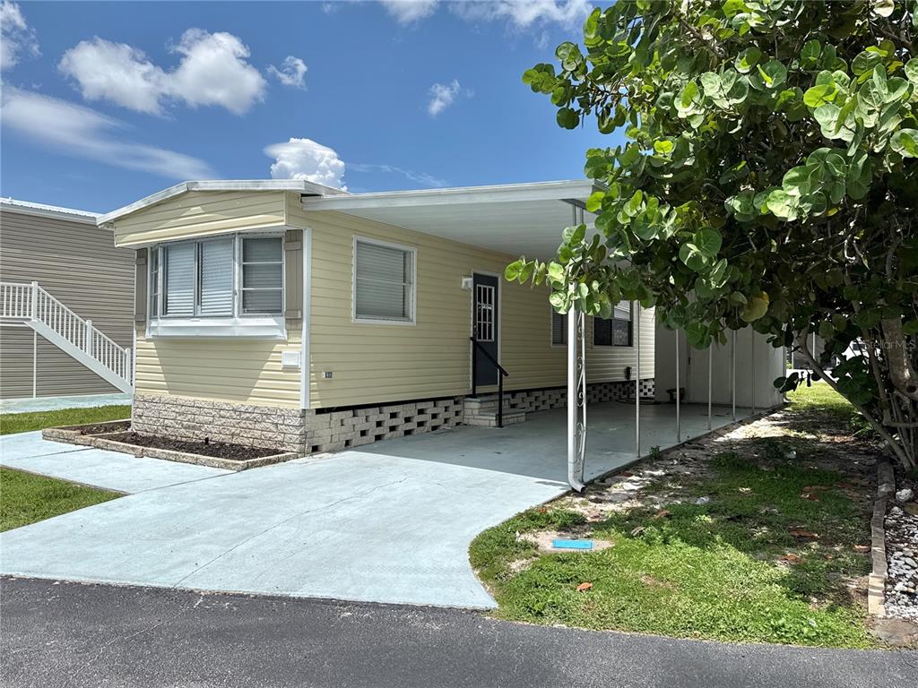 A light yellow mobile home features a concrete driveway, a carport, and a stone-textured base — 347 MOUNT SAXON AVENUE NE UNIT 324, ST PETERSBURG, FL
