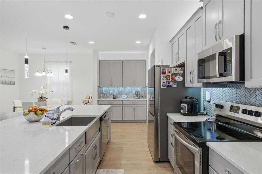A modern kitchen features gray cabinets, white countertops, stainless steel appliances, and a farmhouse sink — 6825 WILSON HAMMOCK AVENUE, GROVELAND, FL