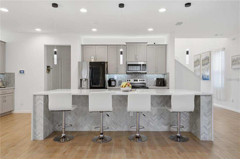 A modern kitchen features a large island with four white bar stools and gray cabinetry — 6825 WILSON HAMMOCK AVENUE, GROVELAND, FL