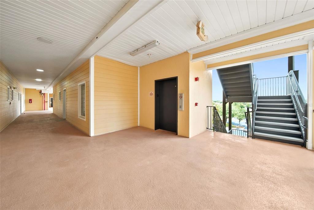 An outdoor apartment hallway features a tan floor, yellow walls, an elevator, and a staircase — 3050 PIRATES RETREAT COURT UNIT 408, KISSIMMEE, FL