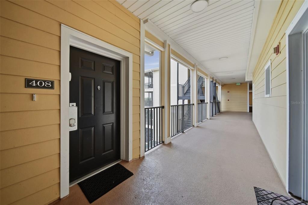 An exterior hallway with a black door labeled 408, yellow siding, and metal railings — 3050 PIRATES RETREAT COURT UNIT 408, KISSIMMEE, FL