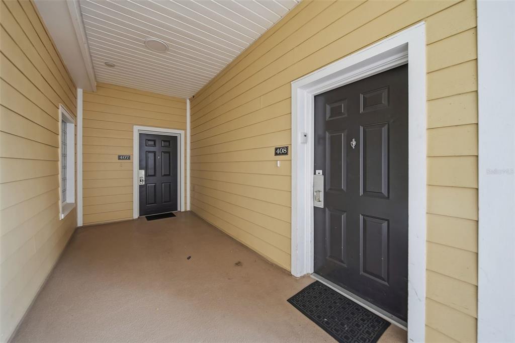 An exterior view of a covered entryway featuring two dark doors numbered 407 and 408 — 3050 PIRATES RETREAT COURT UNIT 408, KISSIMMEE, FL