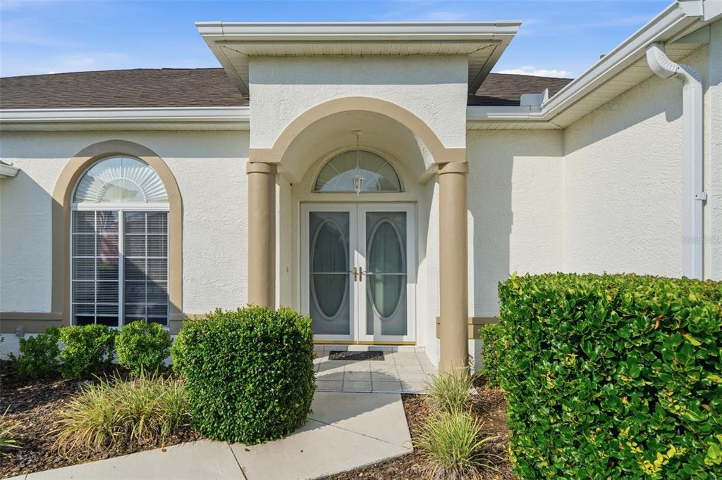 The exterior of a house features a white stucco facade, arched entryway, and double glass doors — 2160 NW 50TH CIRCLE, OCALA, FL