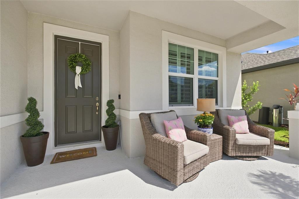 A covered front porch features a dark door, two wicker chairs, and potted spiral topiaries — 8219 TEA OLIVE TERRACE, PALMETTO, FL