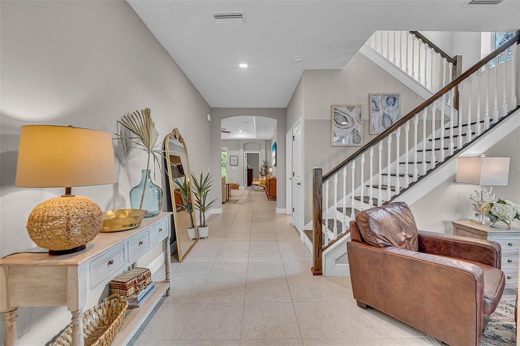 A bright entryway features a staircase, a leather armchair, and a console table with decor — 8219 TEA OLIVE TERRACE, PALMETTO, FL