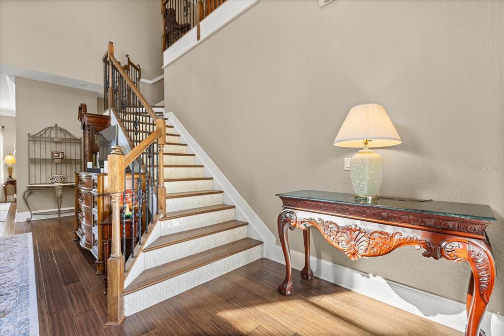 A staircase with patterned risers and a wooden handrail sits beside an ornate console table — 2450 DAHLGREN WAY, WINTER GARDEN, FL