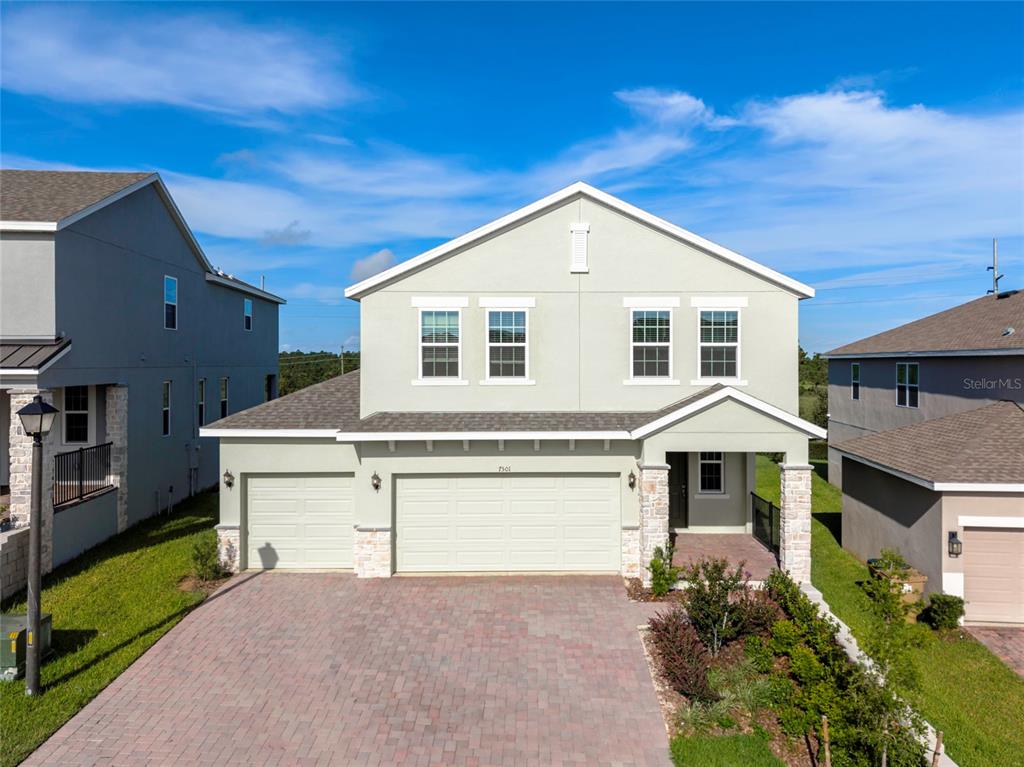 A two-story house with a light green exterior, stone accents, and a paved driveway — 7501 CATANIA LOOP, CLERMONT, FL
