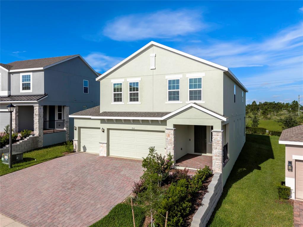 A two-story house with a light-colored stucco exterior, a brick driveway, and a two-car garage — 7501 CATANIA LOOP, CLERMONT, FL
