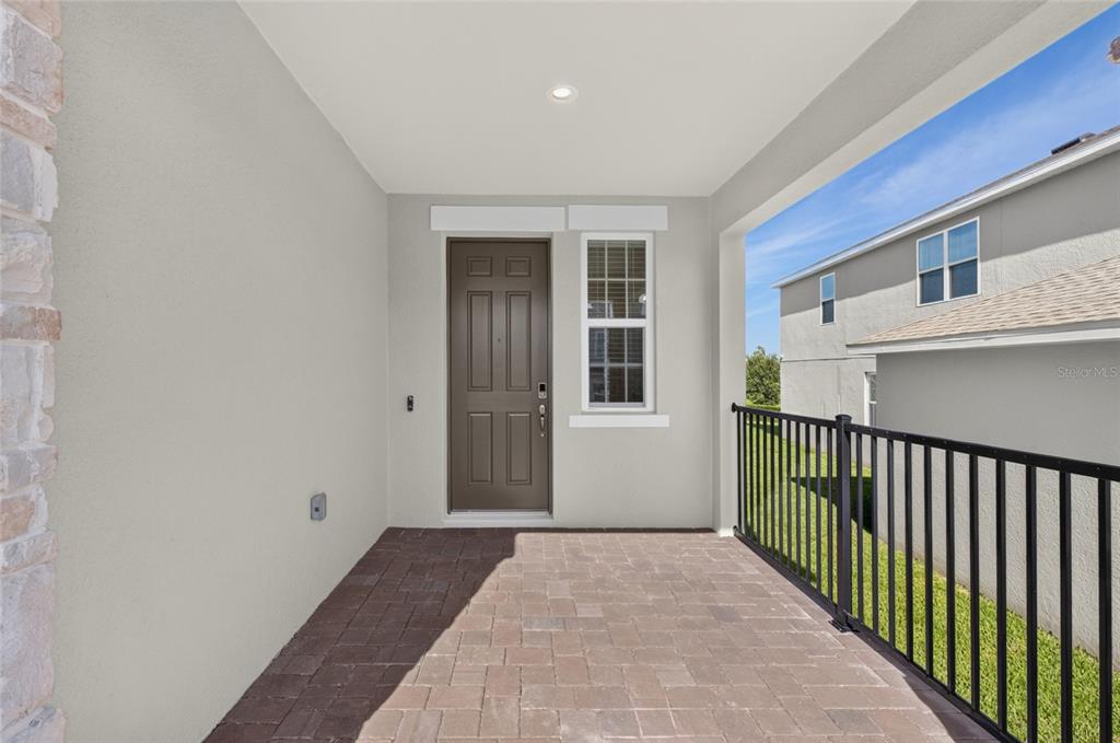 A covered porch features a brown front door, a window, and a black metal railing — 7501 CATANIA LOOP, CLERMONT, FL