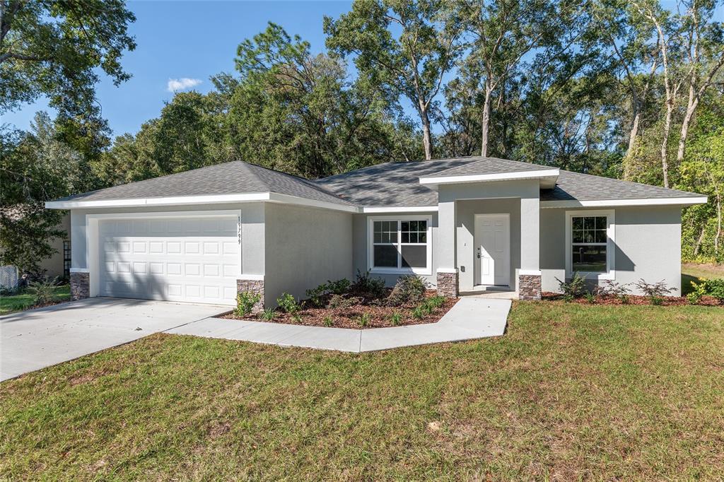 A single-story house with a gray stucco exterior, stone accents, and a two-car garage — 10070 SW 192ND CIRCLE, DUNNELLON, FL
