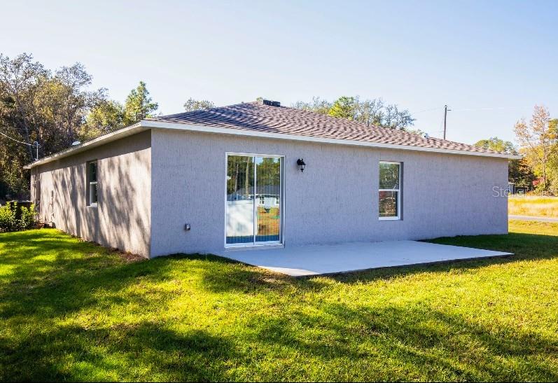 The back exterior of a gray stucco house features a sliding glass door and concrete patio — 16287 MELON ROAD, WEEKI WACHEE, FL
