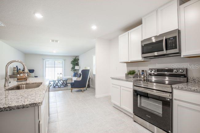 A kitchen with white cabinets, granite countertops, and stainless steel appliances overlooks a living area — 16287 MELON ROAD, WEEKI WACHEE, FL