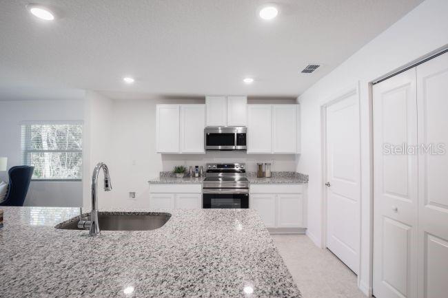A kitchen features white cabinets, granite countertops, a stainless steel sink, and stainless steel appliances — 16287 MELON ROAD, WEEKI WACHEE, FL