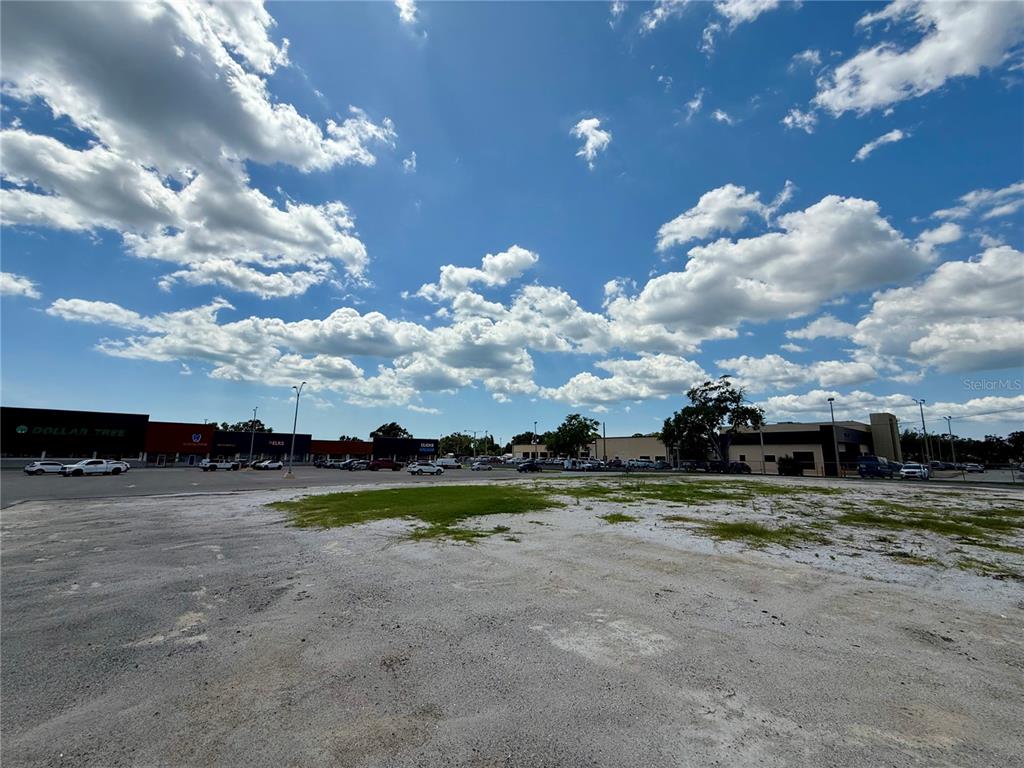 A large, vacant gravel lot sits in front of a strip mall under a cloudy sky — 6812 14TH STREET W, BRADENTON, FL