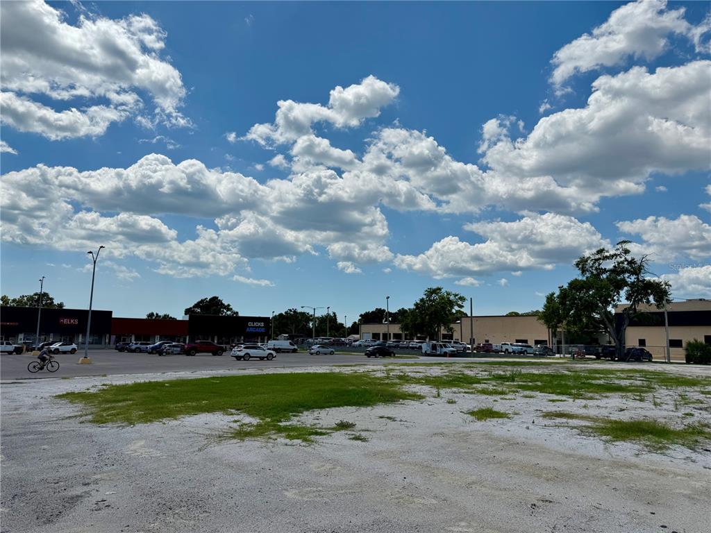 A large, unpaved gravel lot sits in front of a strip mall under a cloudy sky — 6812 14TH STREET W, BRADENTON, FL