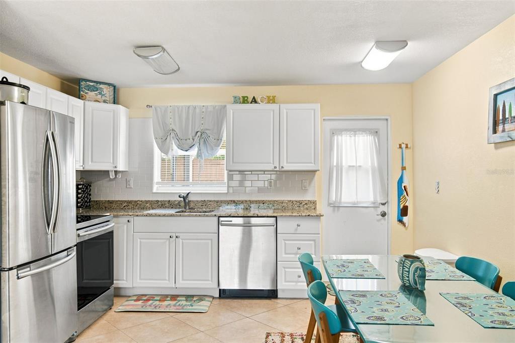 A kitchen features white cabinets, granite countertops, stainless steel appliances, and a dining table — 414 FLUSHING AVENUE, DAYTONA BEACH, FL