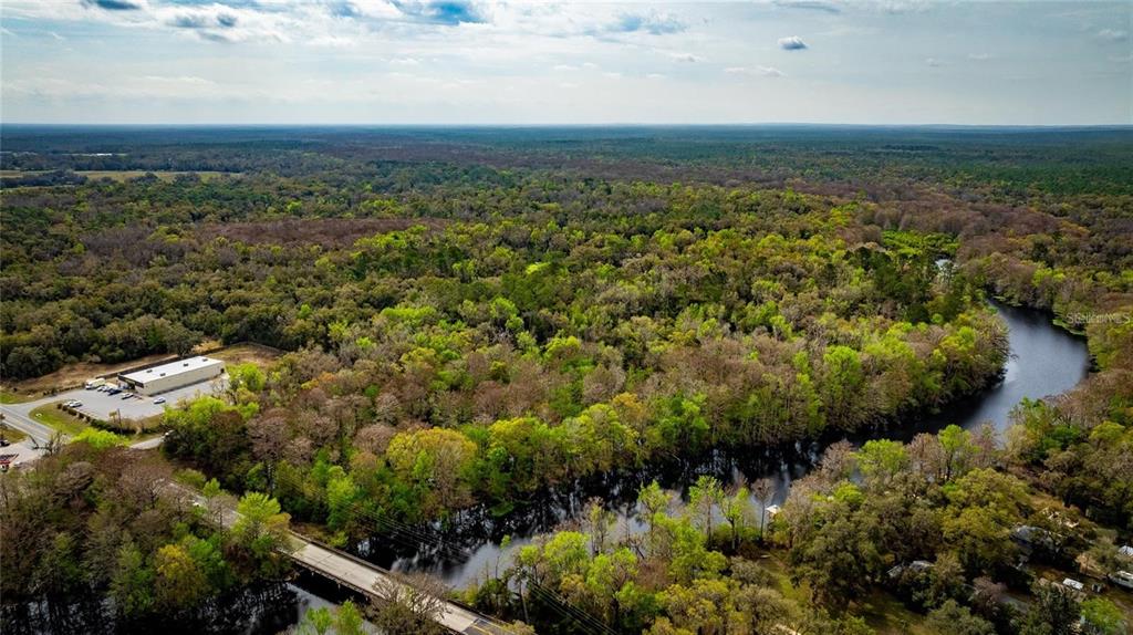 An aerial view shows a river winding through a dense forest near a commercial building — 0 CR 647, BUSHNELL, FL