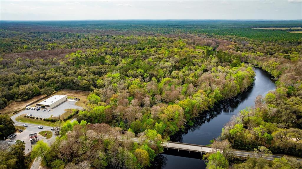 An aerial view shows a commercial building, a bridge, and a river surrounded by forest — 0 CR 647, BUSHNELL, FL