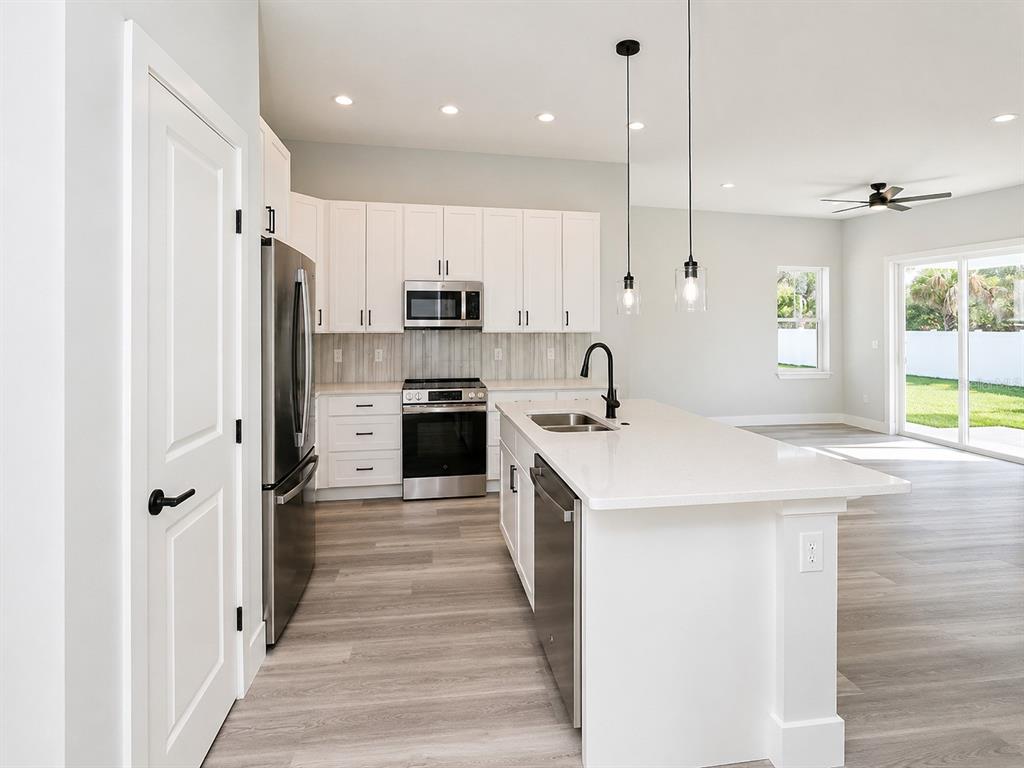 A modern kitchen features white cabinets, stainless steel appliances, a quartz island, and light flooring — 3 WHELAN PLACE UNIT B, PALM COAST, FL