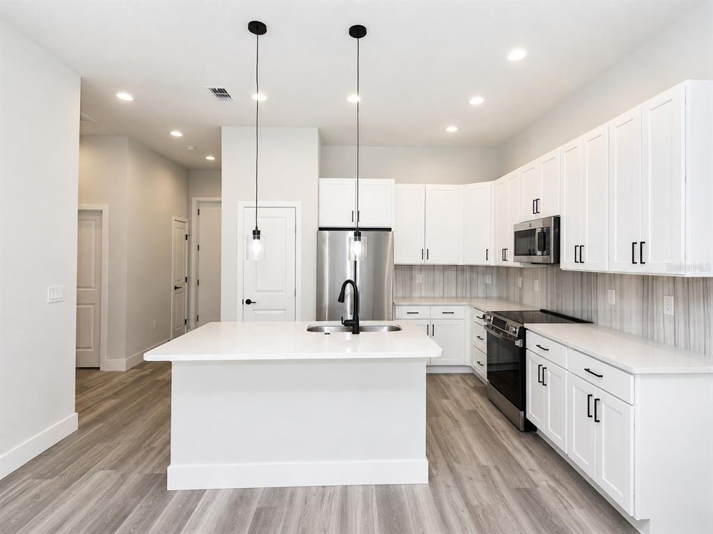 A modern kitchen features white cabinetry, a central island, stainless steel appliances, and wood-look flooring — 3 WHELAN PLACE UNIT B, PALM COAST, FL