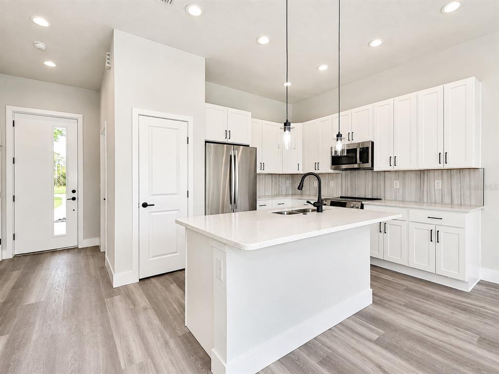 A modern kitchen features white cabinets, a central island, stainless steel appliances, and wood-look flooring — 3 WHELAN PLACE UNIT B, PALM COAST, FL
