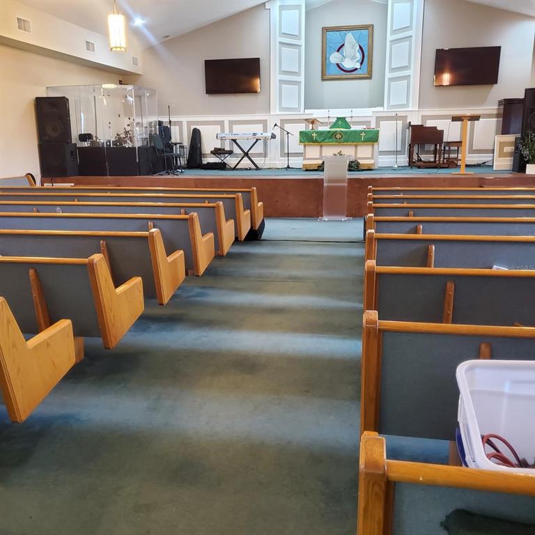 The interior of a church sanctuary features rows of wooden pews facing a raised stage — 1250 PIEDMONT WEKIWA ROAD, APOPKA, FL