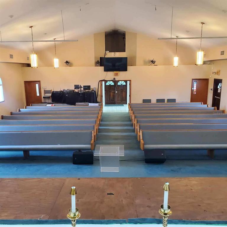 A church sanctuary features rows of grey pews, a central aisle, and a wooden stage — 1250 PIEDMONT WEKIWA ROAD, APOPKA, FL