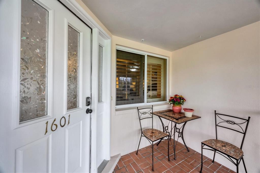 A covered porch features a white front door, a window with shutters, and a bistro set — 11000 PLACIDA ROAD UNIT 1601, PLACIDA, FL