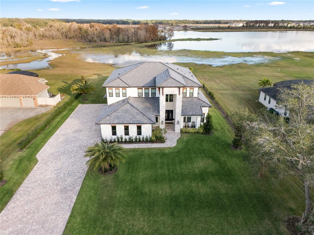 A screened-in swimming pool patio features stone pavers and a sunset view over a lake — 3167 WHISPER WIND DRIVE, ST CLOUD, FL
