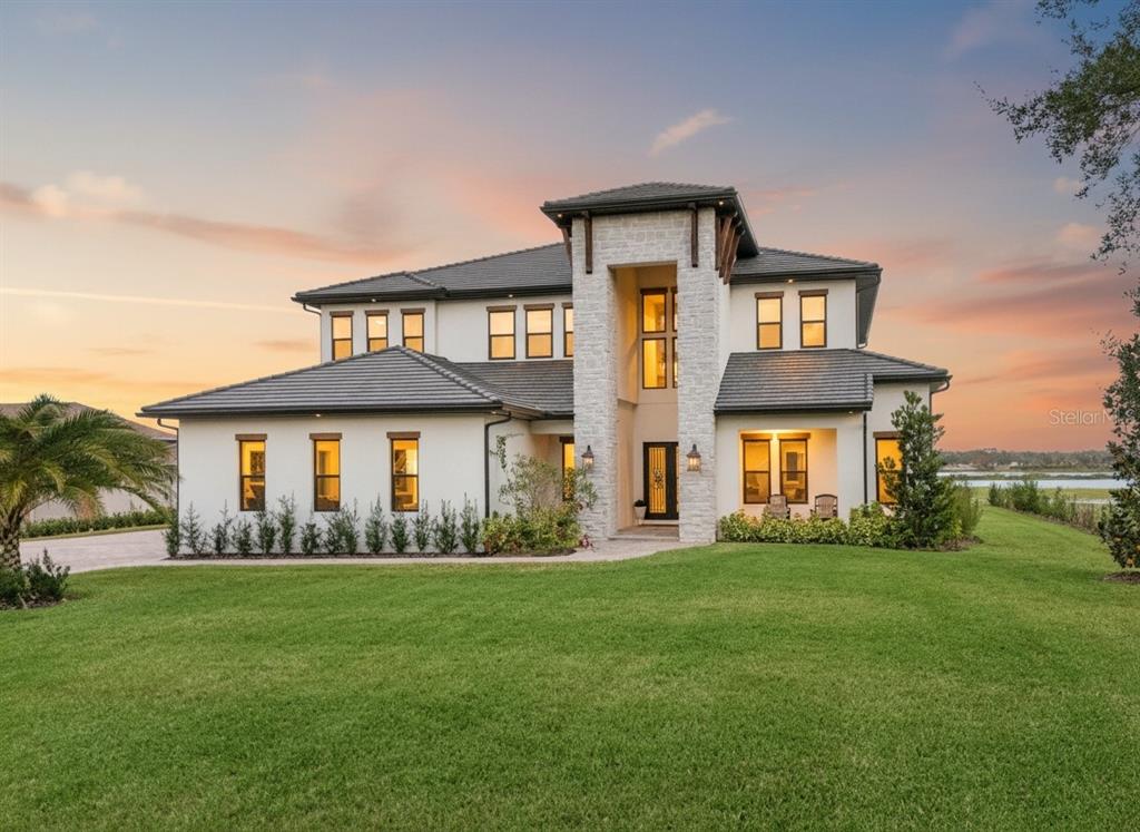 A two-story modern home with a stone-accented entryway and a large front lawn at sunset — 3167 WHISPER WIND DRIVE, ST CLOUD, FL
