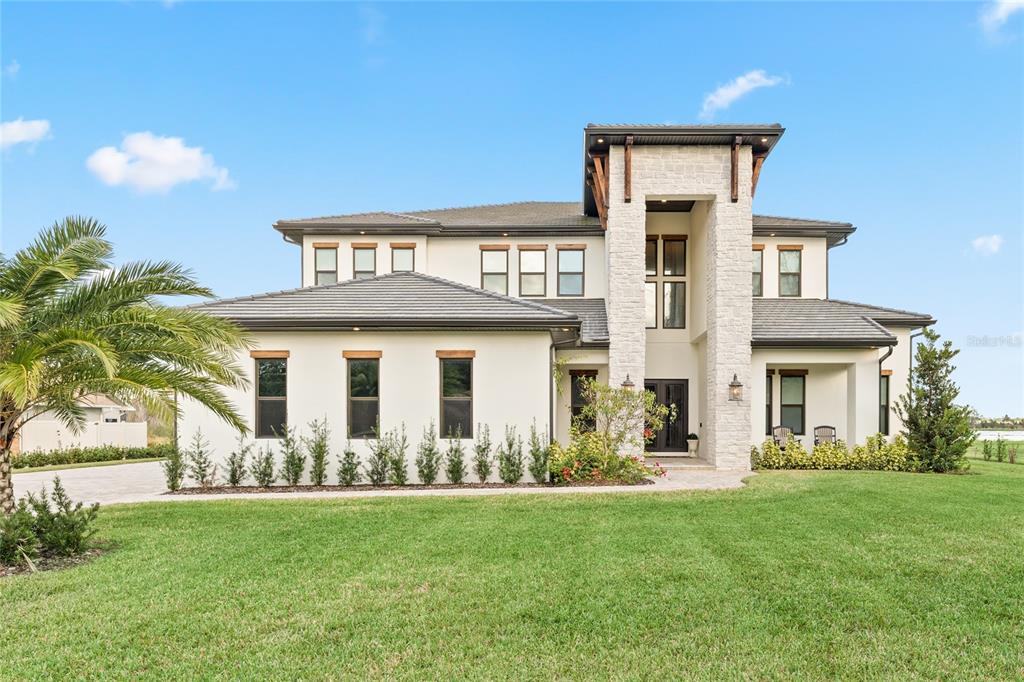 A modern two-story house with a stone-accented entryway and a large green lawn — 3167 WHISPER WIND DRIVE, ST CLOUD, FL